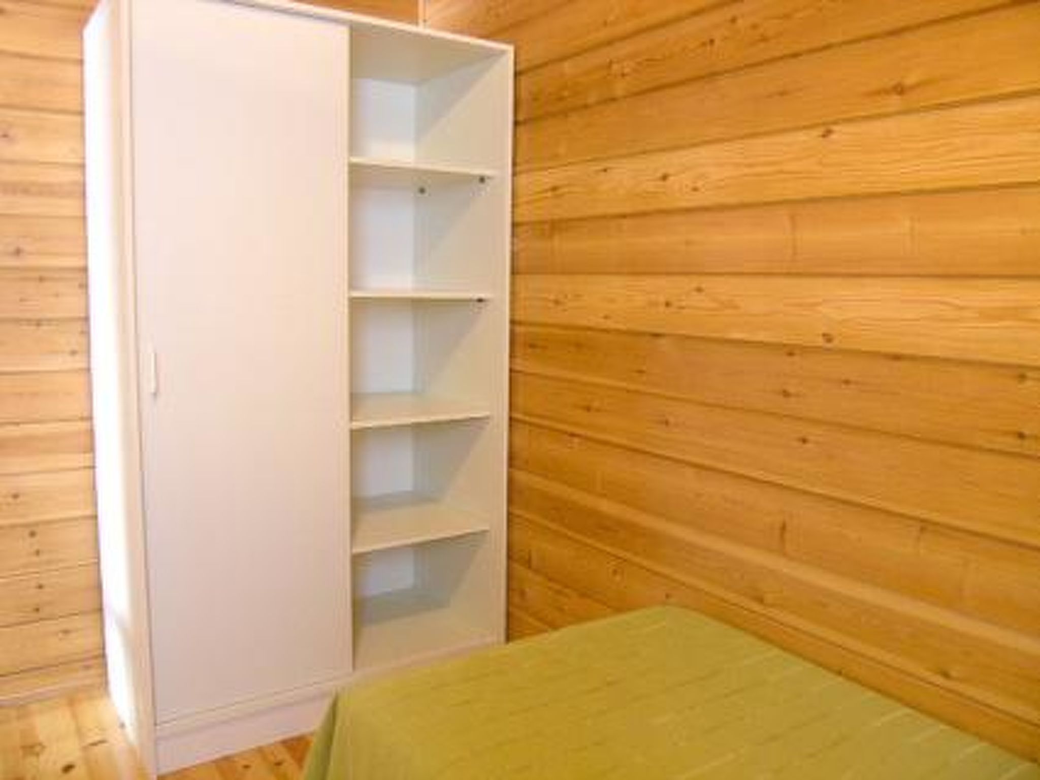 A room with a white wardrobe with multiple shelves, a green bed, and wooden walls.