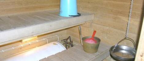A small, wooden cabin with a metal sink, a blue container, and a metal bucket with a red spoon.