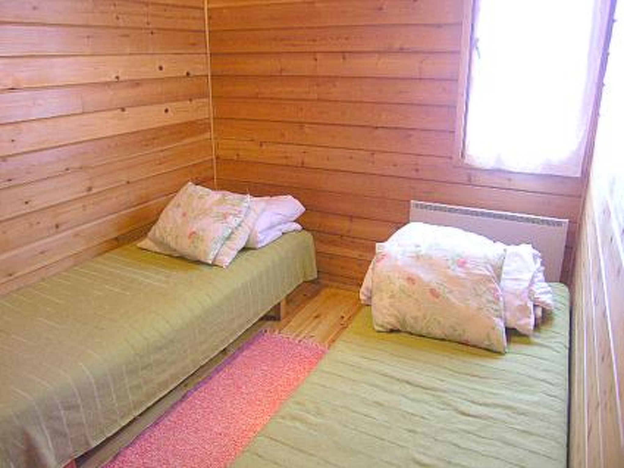 A small, single-room cabin with two beds, each with a pillow and a green bedspread.