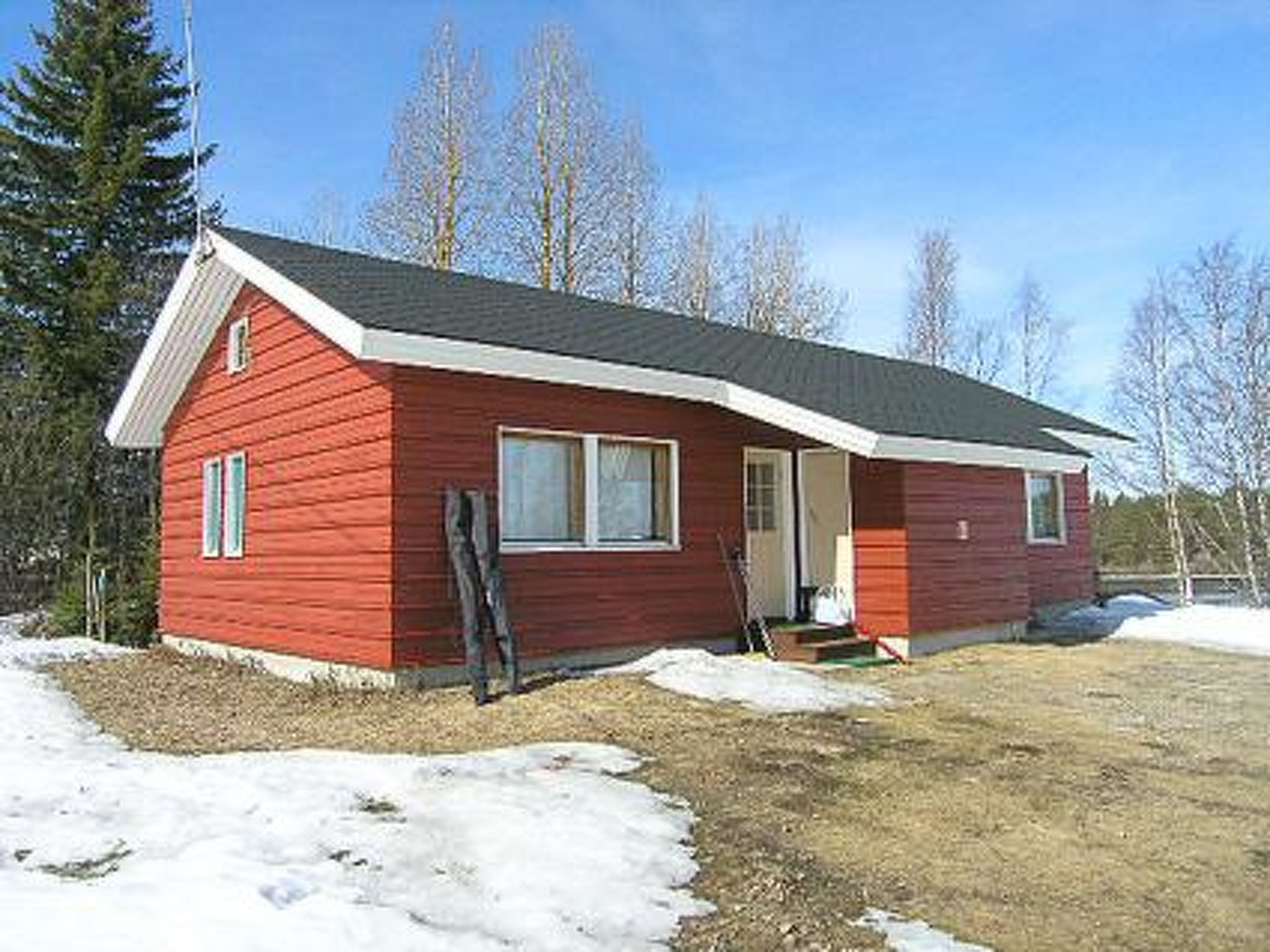 Eine kleine, einstöckige rote Holzhütte mit Satteldach, einer Veranda und einer sichtbaren Tür.