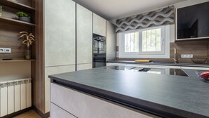 A modern kitchen with a large island, built-in appliances, and a window with decorative curtains.