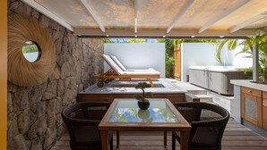 A covered outdoor area with a stone wall, lounge chairs, a hot tub, and a table with chairs. - Lodge Freedom      . (La Grande Saline)