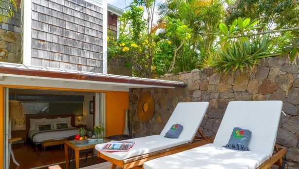 A wooden deck with two sun loungers, a stone wall, and a room with a bed and a table. - Lodge Freedom      . (La Grande Saline)