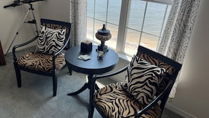 Quarto com telescópio, cadeiras com padrão de zebra, uma pequena mesa com objetos decorativos e vista para o mar através de grandes janelas.