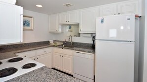 Una cocina con armarios blancos, encimera de granito, estufa, fregadero y refrigerador.