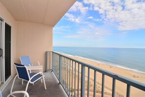 A balcony with two white chairs and a table, overlooking a beach with a clear sky and calm sea. - OCEAN FRONT CONDO.  ENJOY YOUR MORNING COFFEE SITTING ON YOUR PRIVATE BALCONY WATCHING THE SUNRISE. (Rehoboth Beach)