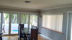 A spacious living area with a large dining table, comfortable seating, and a view of a pool through large windows. - Bamboo Beach House! (Redington Beach)