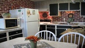 Een kleine keuken met een koelkast, magnetron en fornuis. Er is een eettafel met stoelen en een bloevas.