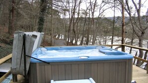 Een hottub op een houten terras met uitzicht op een bebost gebied en een waterlichaam.
