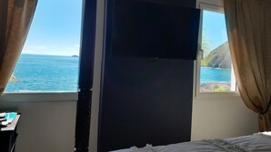 Ein Zimmer mit einem Bett, einem an der Wand befestigten Fernseher und einem Fenster mit Vorhängen.