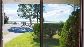 A view from a window overlooking a well-maintained lawn, a tree, and a body of water in the distance. - Beachside Shoal Bay Unit 2 (Shoal Bay)
