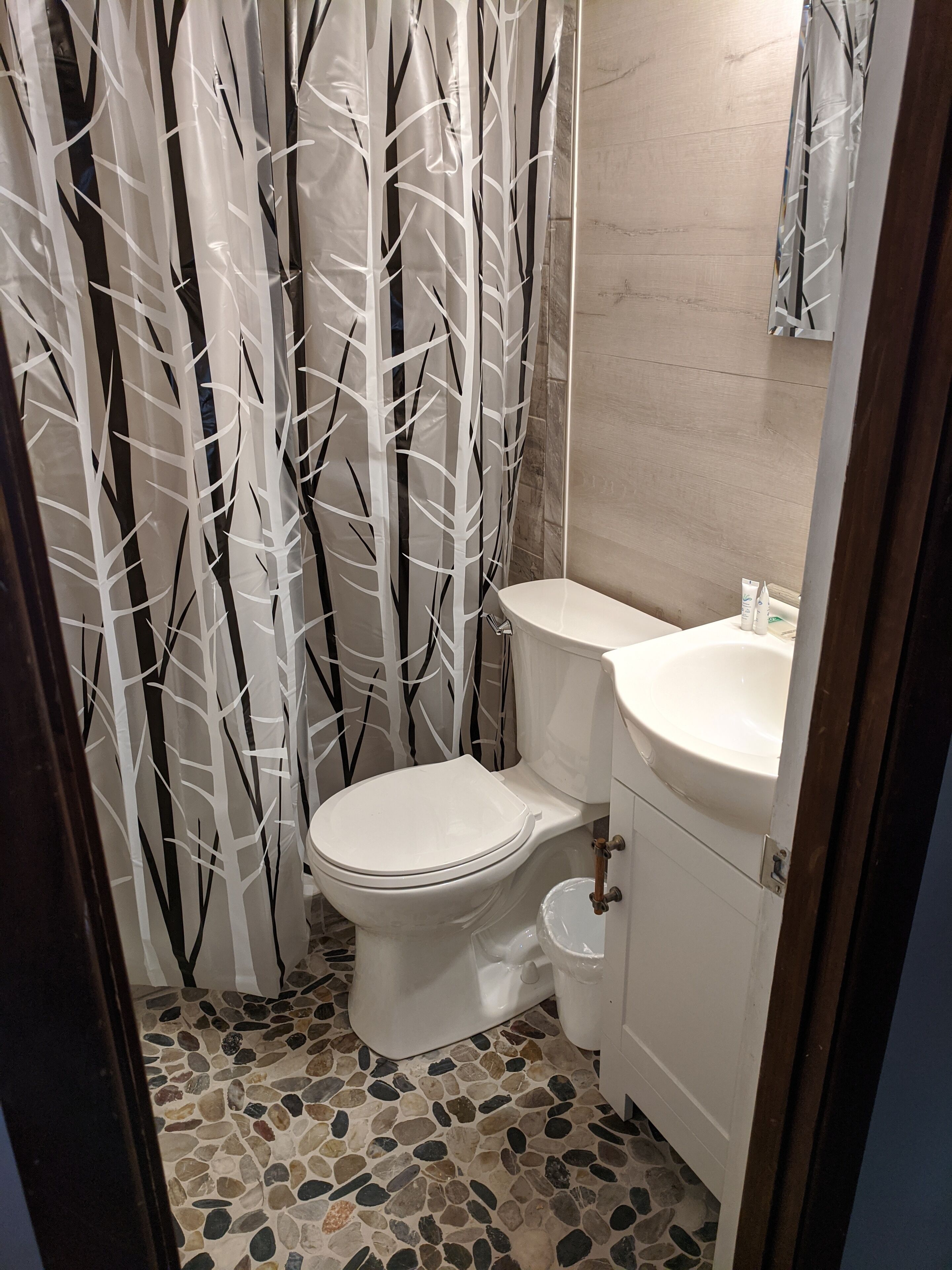 Een badkamer met toilet, wastafel en een douchegordijn met een boommotief.