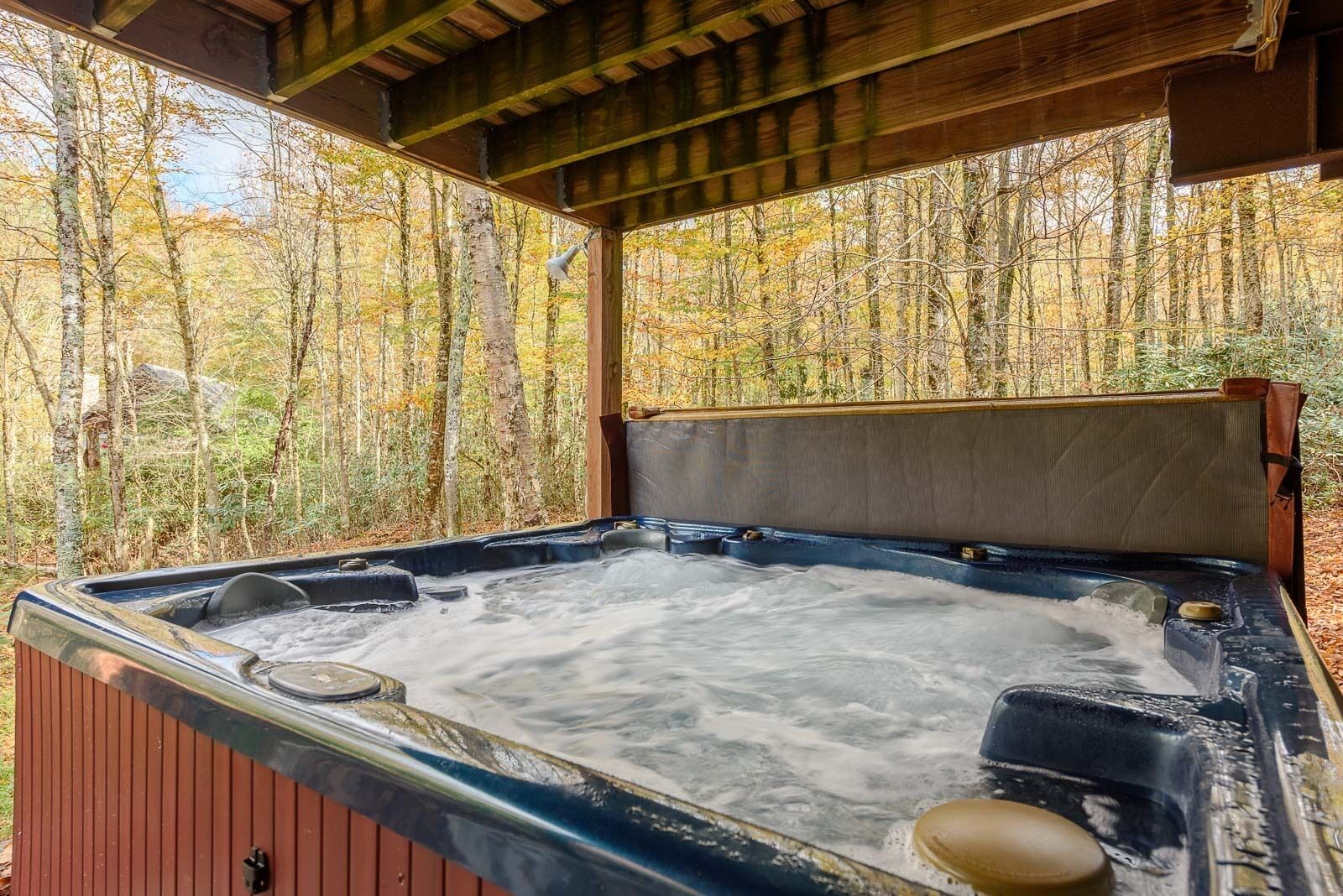 A hot tub with a wooden bench and a metal cover, surrounded by trees.
