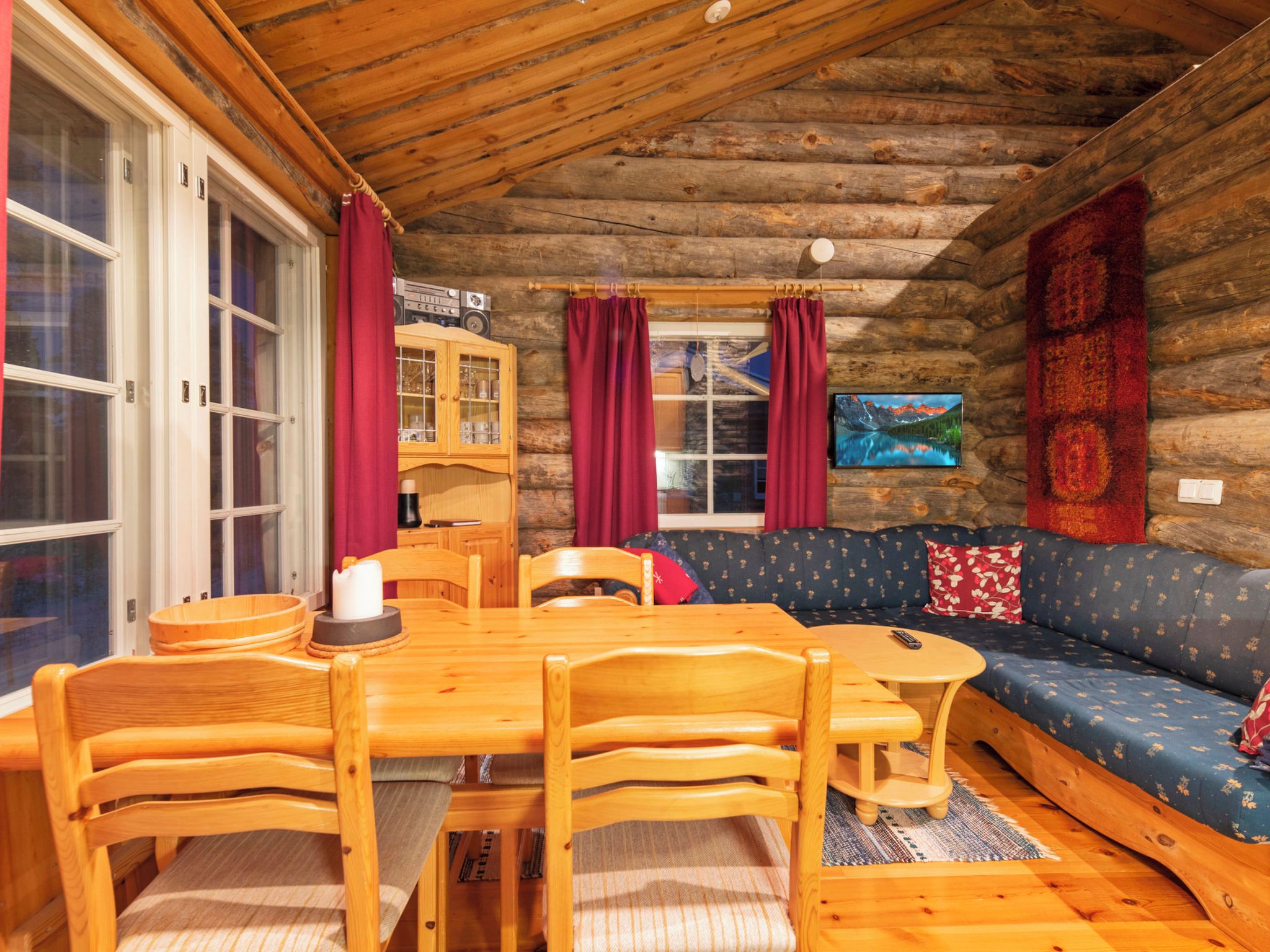 A log cabin interior with a dining table, chairs, a sofa, and a television.