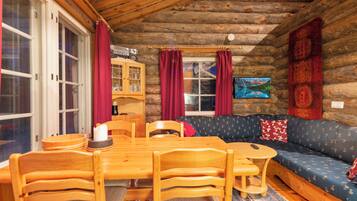 A log cabin interior with a dining table, chairs, a sofa, and a television.