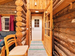Interior de una cabaña de madera con una silla, un sofá y una puerta que da a otra habitación.