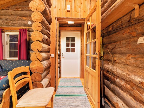 Interior de una cabaña de madera con una silla, un sofá y una puerta que da a otra habitación.
