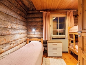 Una habitación tipo cabaña de madera con una cama, un escritorio y una ventana con cortinas.