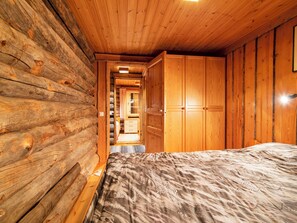 A log cabin interior with a bed, wooden walls, and a door leading to a hallway.