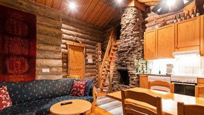 A cozy log cabin interior with a sofa, a round wooden table, and a kitchen area.