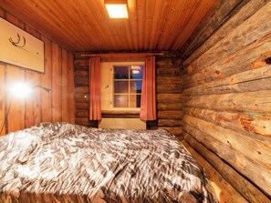 Habitación tipo cabaña de madera con una cama, una ventana con cortinas y una lámpara fijada a la pared.