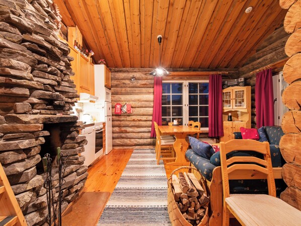A cozy log cabin interior with a stone wall, wooden furniture, and a dining area.