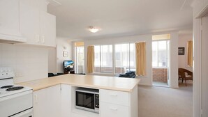 Eine moderne Küche mit weißen Schränken, einem eingebauten Backofen und einer Mikrowelle. Es gibt einen Essbereich mit Tisch und Stühlen sowie ein großes Fenster mit Vorhängen.