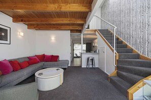 A modern interior with a wooden ceiling, grey sofa with red cushions, a white coffee table, and a staircase with a white railing. - Just the Spot,  a 500m stroll to Queenstown CBD (Queenstown)