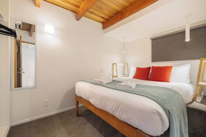 A bedroom with a wooden bed frame, white bedding, and a green throw blanket.