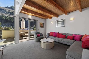A modern living room with a grey sofa, red cushions, a round coffee table, and a glass door leading to an outdoor patio. - Just the Spot,  a 500m stroll to Queenstown CBD (Queenstown)