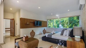 Un salón moderno con un sofá, un televisor montado en la pared y un ventanal con vistas a zonas verdes.