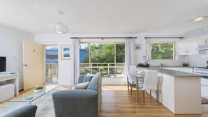 Een moderne keuken met witte kasten, een eethoek met een glazen tafel en een grijze bank.