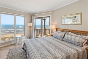 A bedroom with a large bed, a view of the beach, and a balcony with a railing.