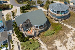 A large house with a curved roof, a deck with outdoor furniture, and a circular structure with a roof.