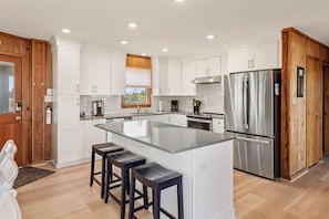 Una cocina moderna con armarios blancos, un refrigerador de acero inoxidable e una isla central con taburetes de bar.
