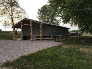 A single-story building with a covered porch, a gravel driveway, and a grassy area. - The Lodge at 5J Hunts (Carrollton)