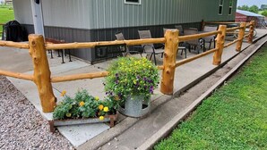 A rustic building with a wooden fence, outdoor seating, and flower planters. - The Lodge at 5J Hunts (Carrollton)