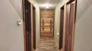 A hallway with wooden flooring and doors on both sides, leading to a room with a wooden wall and a light fixture on the ceiling. - The Lodge at 5J Hunts (Carrollton)