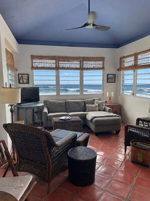 A living room with a view of the ocean, a ceiling fan, and a television. - BEACH HOUSE W/ POOL (vieques)