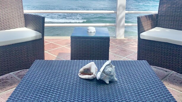 A seaside patio with wicker furniture and a table, overlooking the ocean. - BEACH HOUSE W/ POOL (vieques)