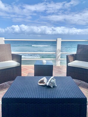 A seaside patio with wicker furniture and a table, overlooking the ocean. - BEACH HOUSE W/ POOL (vieques)