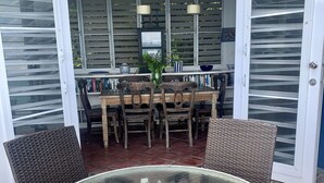 An outdoor patio area with a round glass table, wicker chairs, and a wooden dining table with chairs. - BEACH HOUSE W/ POOL (vieques)