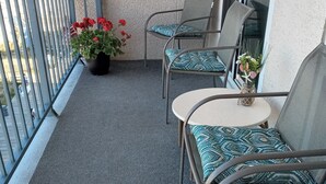 Un balcon avec vue sur l’océan, un pot de fleurs orné de fleurs rouges et un coin salon agrémenté de coussins à motifs.