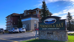 A sign for Peninsula Bay Resort Condominiums with a stone base and a logo depicting a mountain and water.