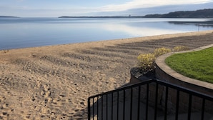 A beach with a calm lake, a grassy area, and a stone pathway.