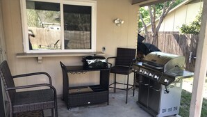 Terrassa exterior amb una barbacoa, dues cadires de vimet i una finestra amb vista a un pati.