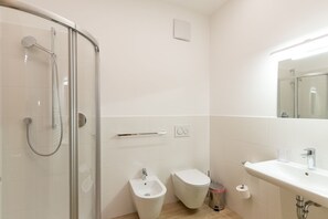 Bathroom features a glass-enclosed shower, bidet, and toilet, with a large mirror above the sink.