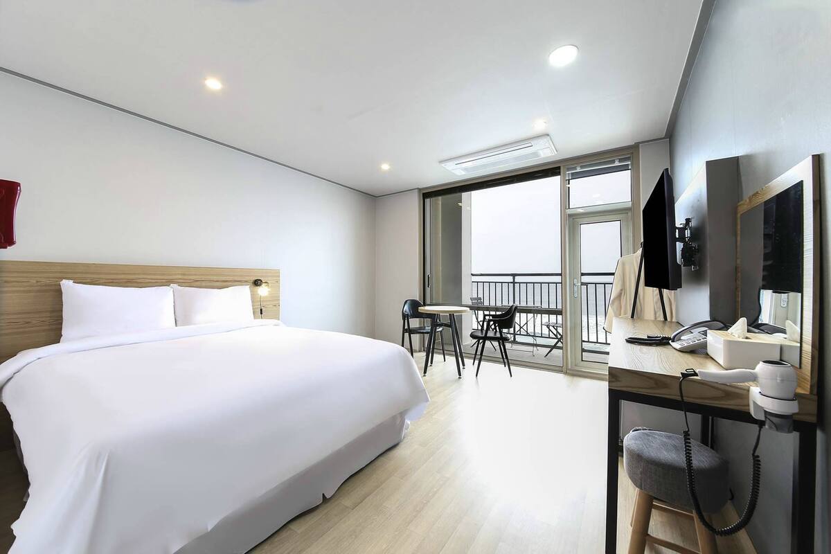 A hotel room with a large bed, a desk with a telephone, and a balcony with chairs.