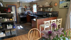 A kitchen with a central island, wooden chairs, and a dining table with a floral tablecloth. - Classy AF Home Steps from Colby and Trails (Oakland)
