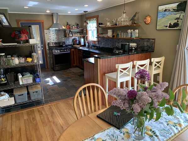 A kitchen with a central island, wooden chairs, and a dining table with a floral tablecloth.